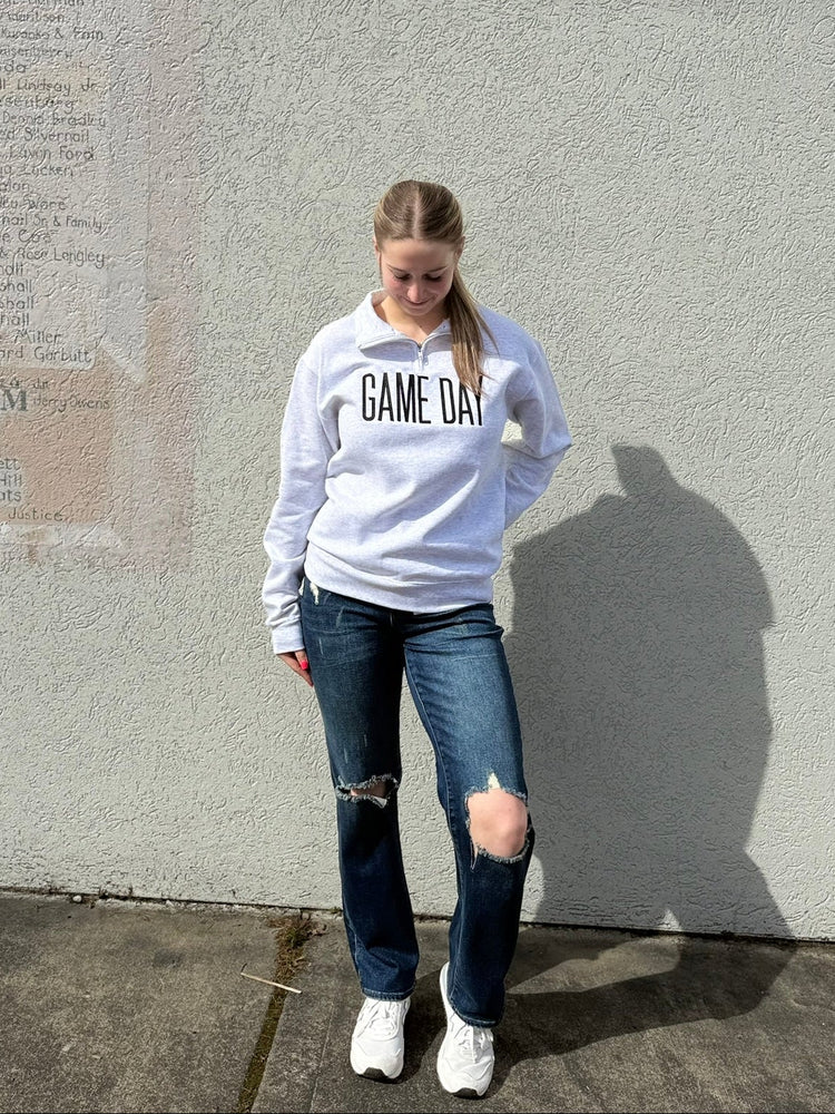 Person wearing a 'Game Day' sweatshirt standing against a gray wall.